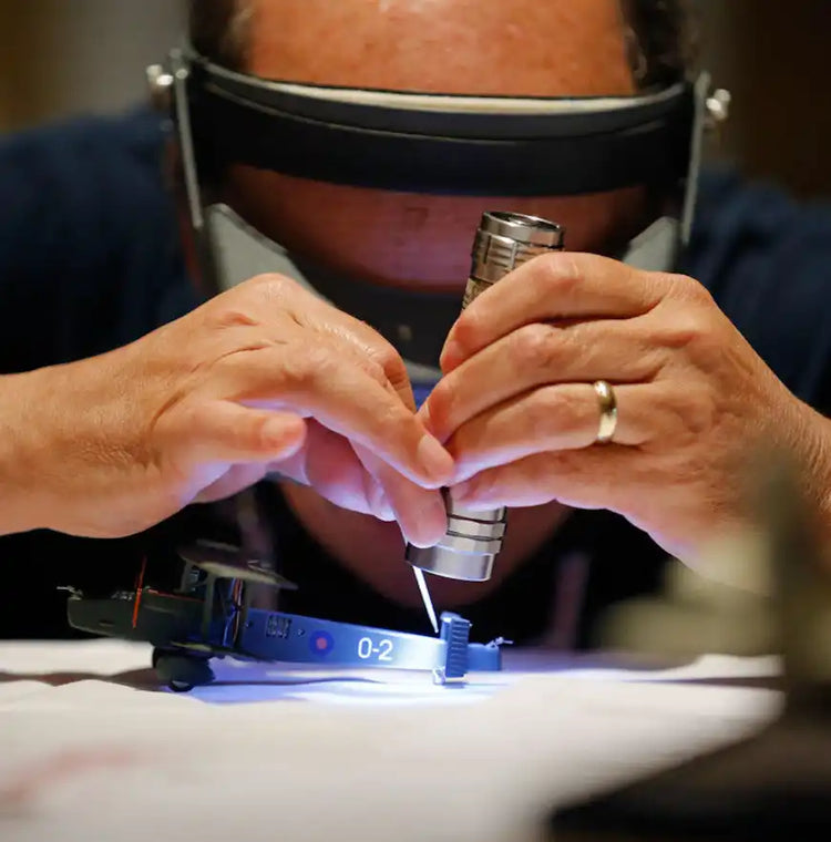 Hands wearing protective eyewear while working with a soldering iron on electronics.