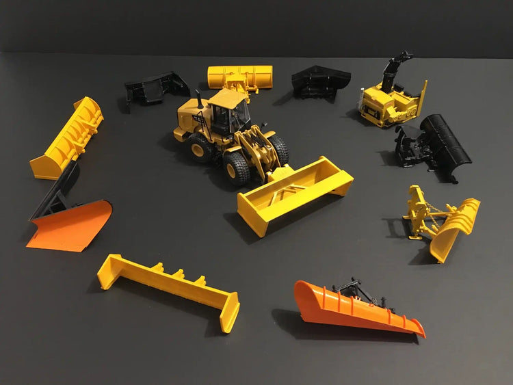 Yellow construction loader with various detachable bucket and blade attachments scattered around it.